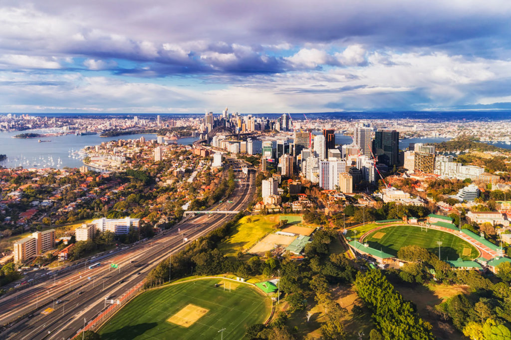 North Sydney oval with North Sydney high-rise towers along Warringah freeway and further down to SYdney harbour with city CBD in elevated aerial view.